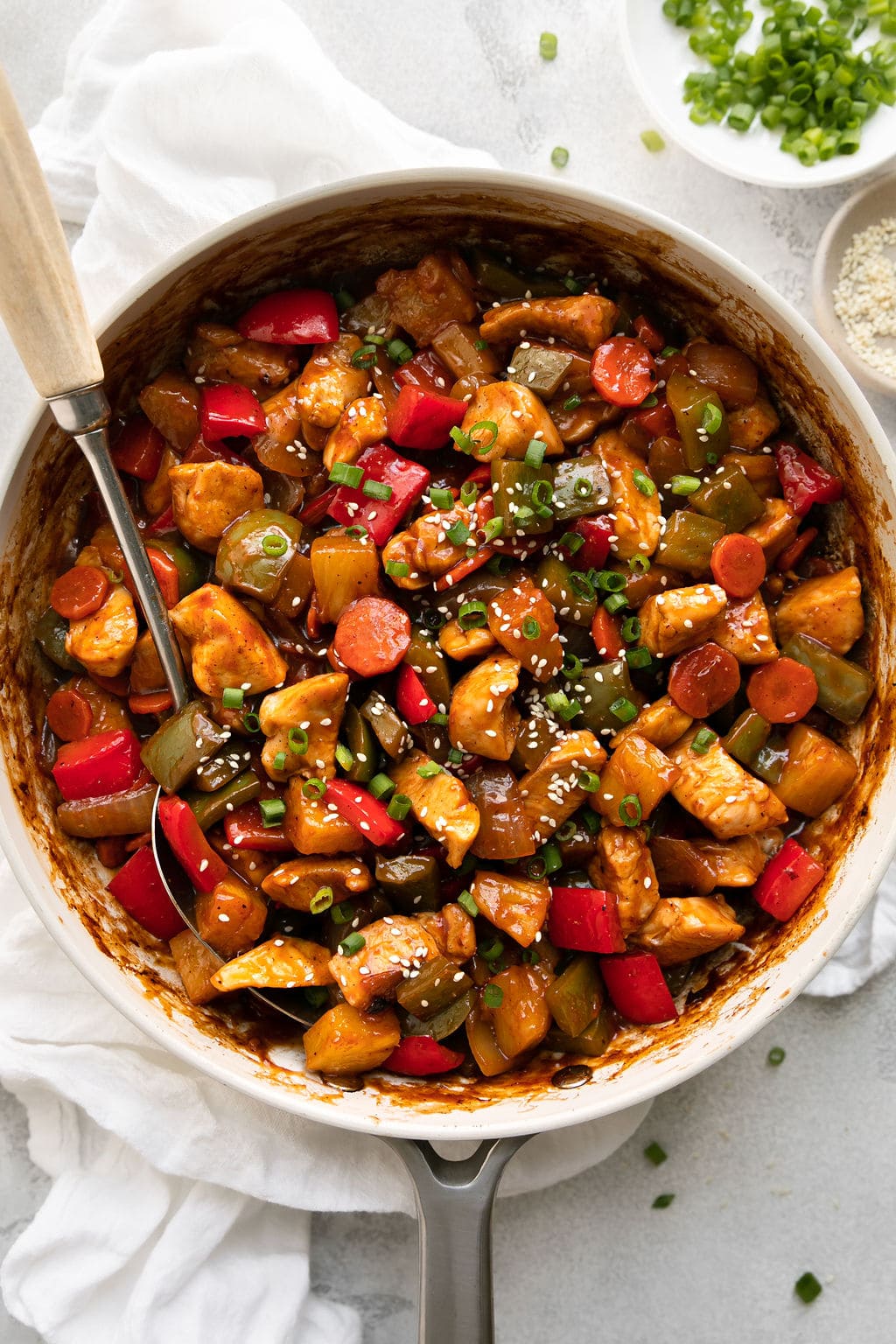 Overhead view white skillet filled with sweet and sour chicken, serving spoon in chicken