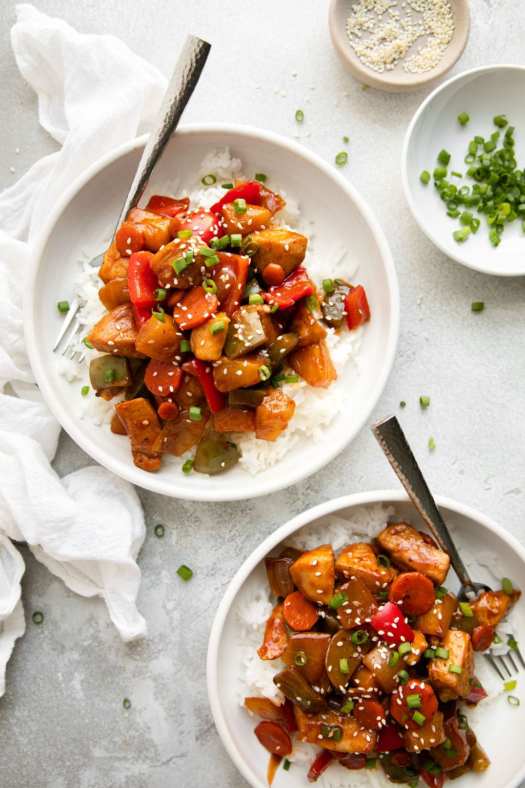 Two white bowls filled with servings of sweet and sour chicken over rice