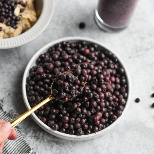 Gold spoon with spoonful of wild blueberries over stone bowl filled with berries