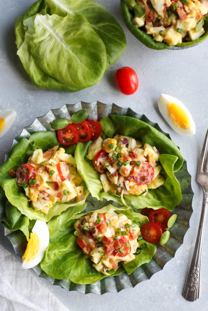 Overhead view lettuce leaves filled with BLT egg salad mixture on silver tray.