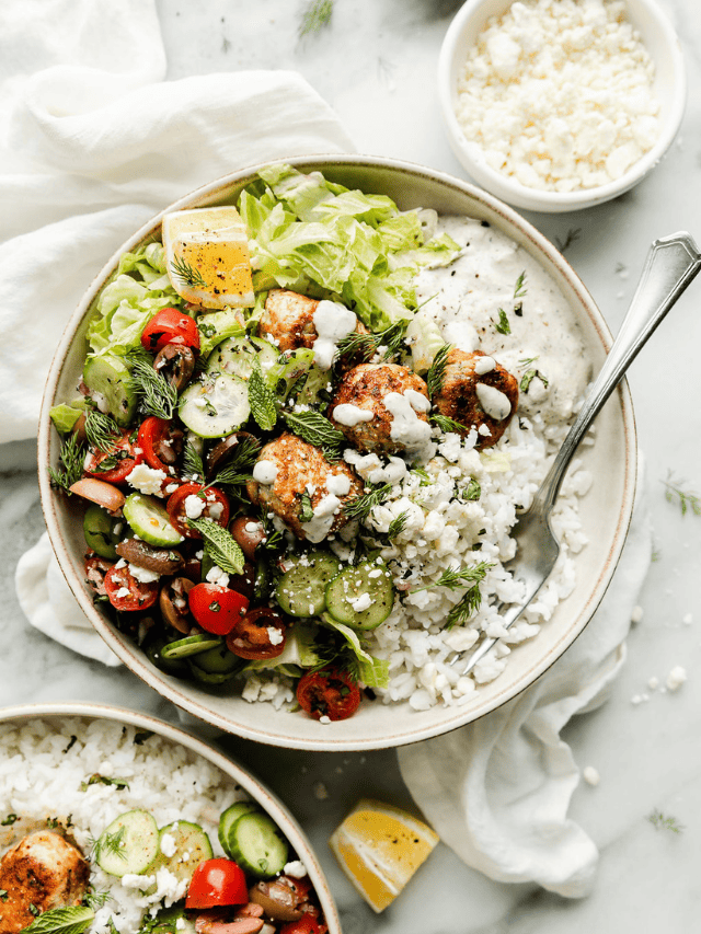 Close up view of a bowl of Greek chicken meatballs topped with tzatziki sauce. 