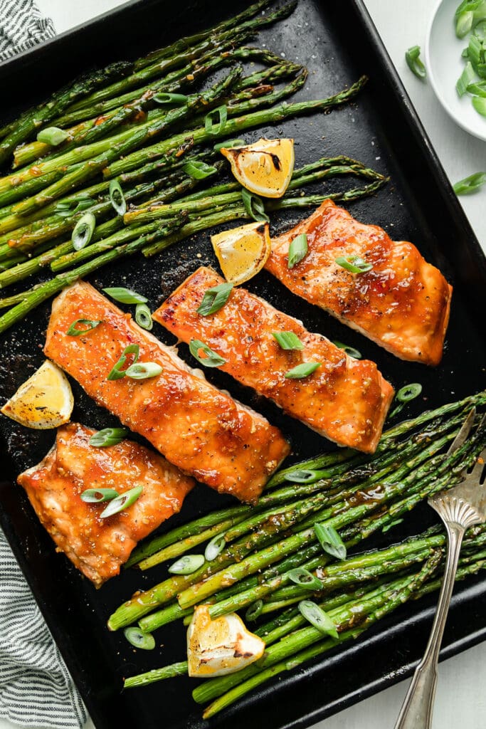 Overhead view sheet pan filled with glazed salmon filets and roasted asparagus with lemon wedges