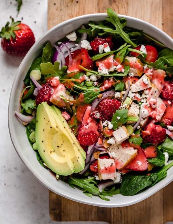 Overhead view serving bowl filled with strawberry spinach salad topped with avocado slices and strawberry vinaigrette