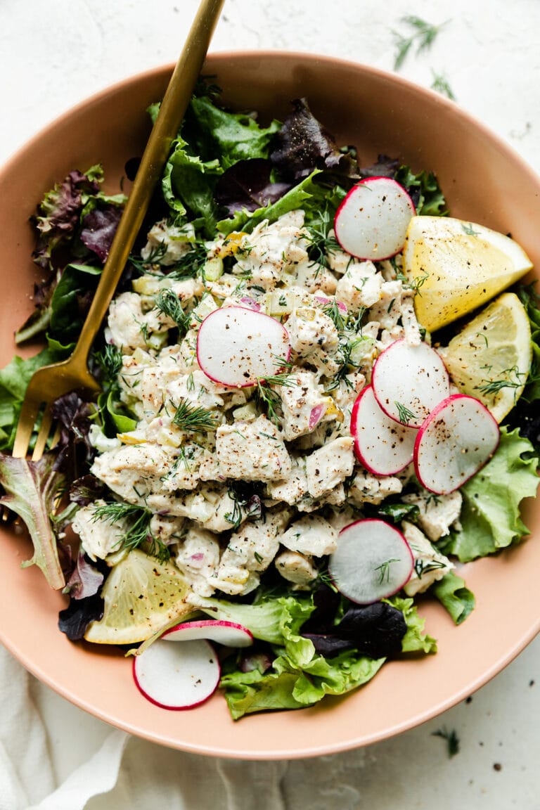Close up view of a bowl of dill pickle chicken salad topped with finely sliced radishes. 