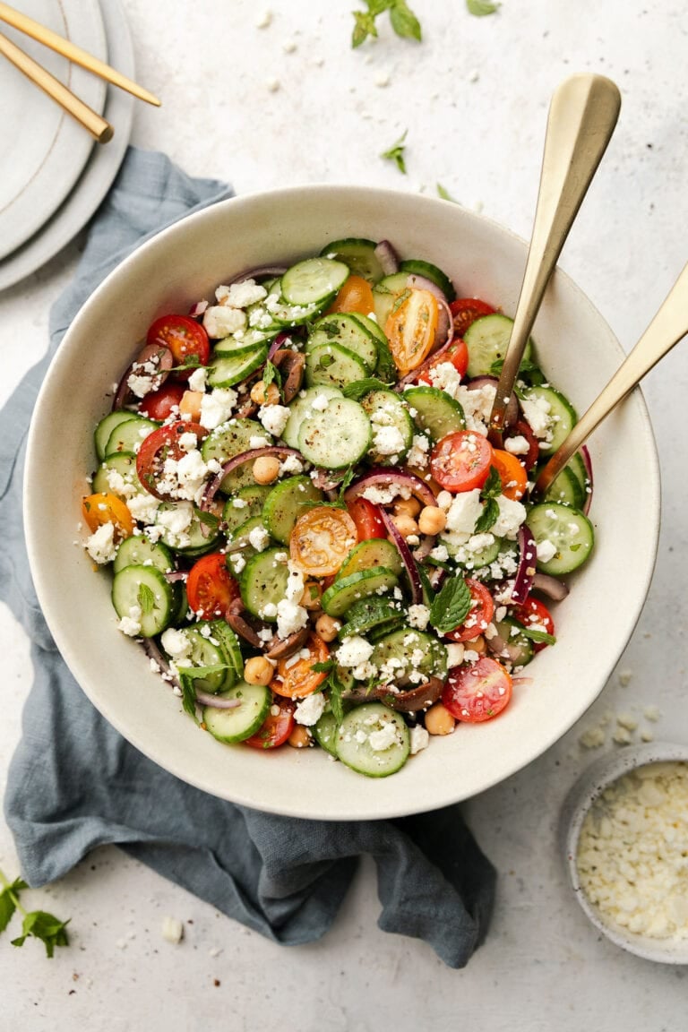 Close up view of a white bowl of chopped Greek salad with quick marinated cucumbers, red onion, and tomatoes with chickpeas, kalamata olives, and crumbled feta.