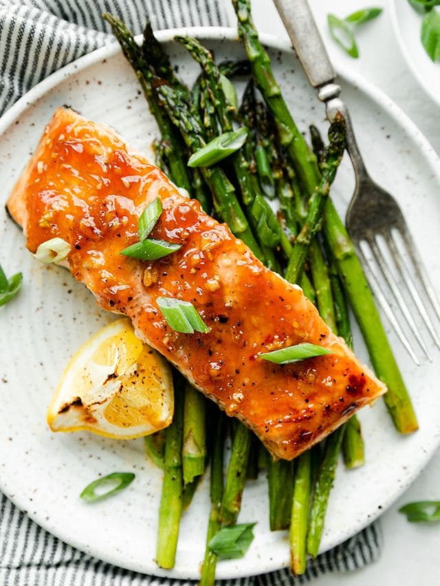 An overhead view of honey glazed salmon on a plate with asparagus and lemon.