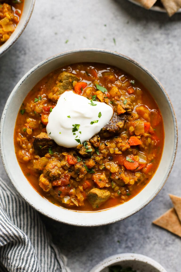 Overhead view of a bowl of Moroccan Beef and Lentil Stew topped with a dollop of yogurt and fresh herbs. 