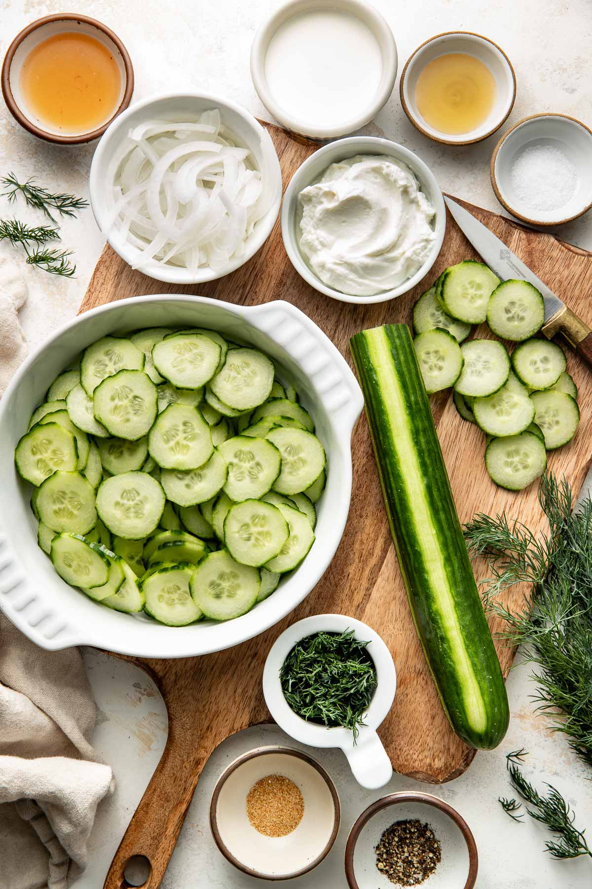 Overhead view of a variety of ingredients for cucumber salad in different sized bowls.