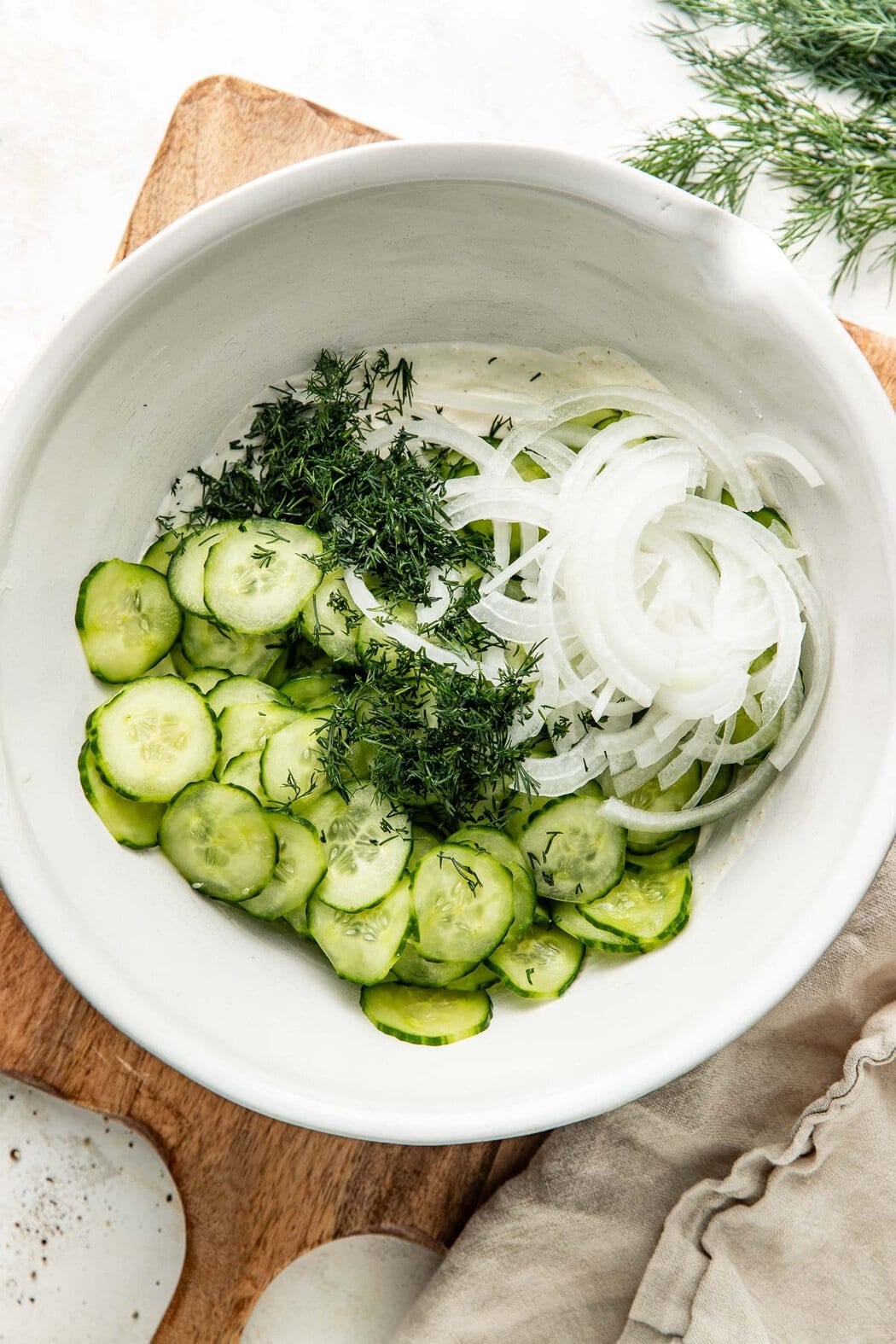 Overhead view of cucumber salad ingredients in a bowl arranged in sections.