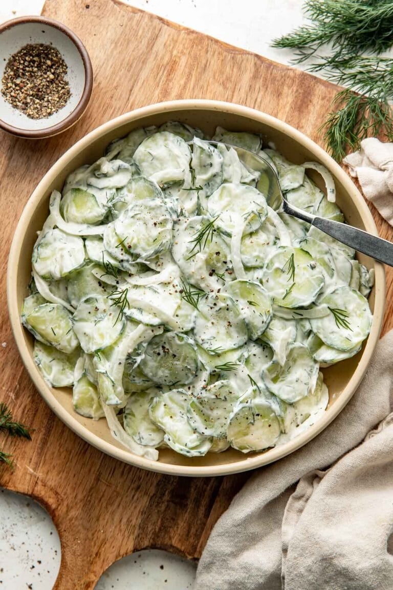 Overhead view of a bowl filled with creamy cucumber salad topped with fresh dill and black pepper.
