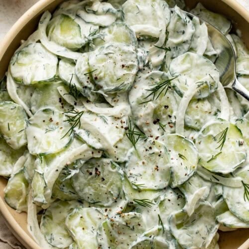 Overhead view of a bowl of creamy cucumber salad topped with fresh dill and black pepper.