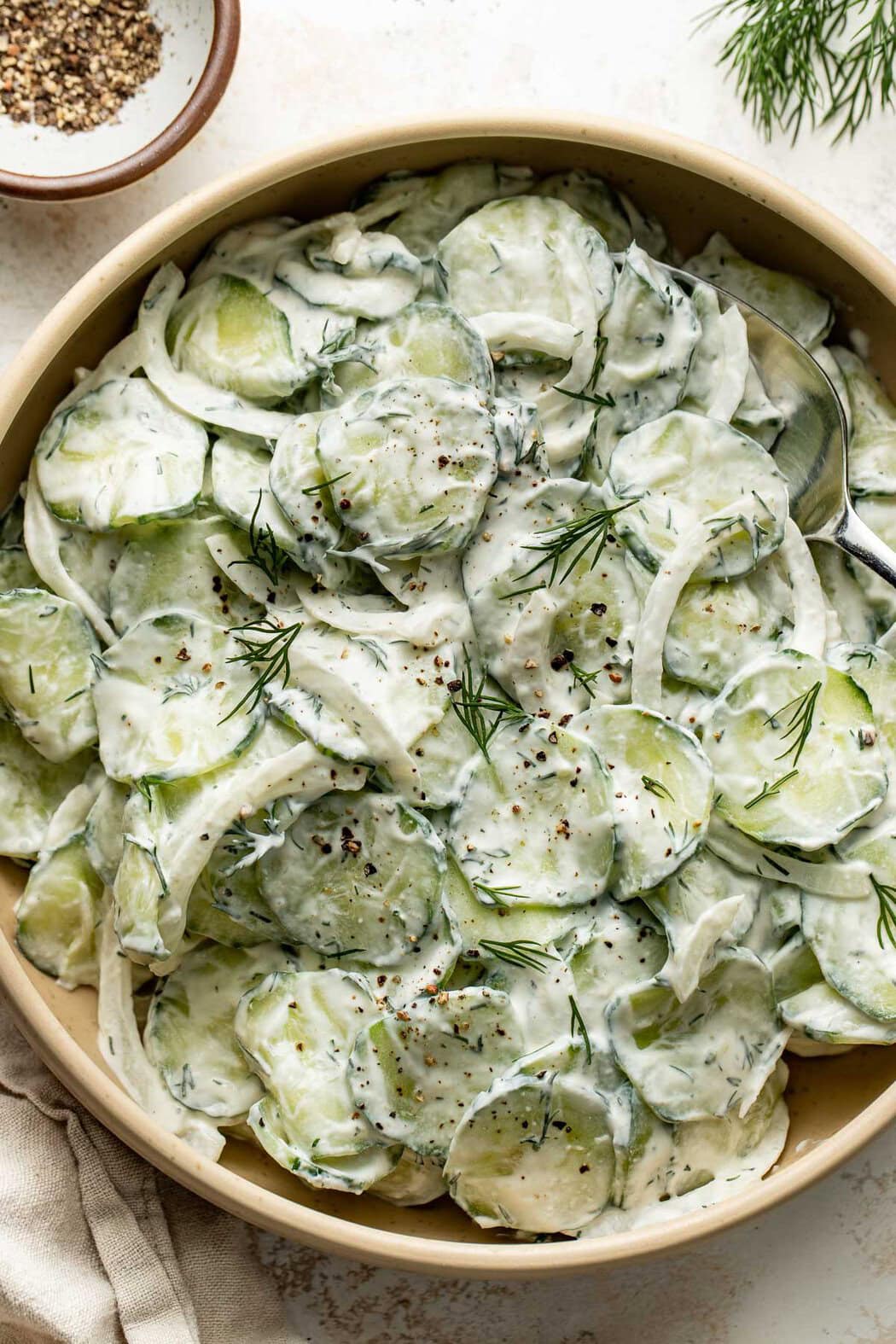Overhead view of a bowl of Creamy Cucumber Salad topped with fresh dill and black pepper.