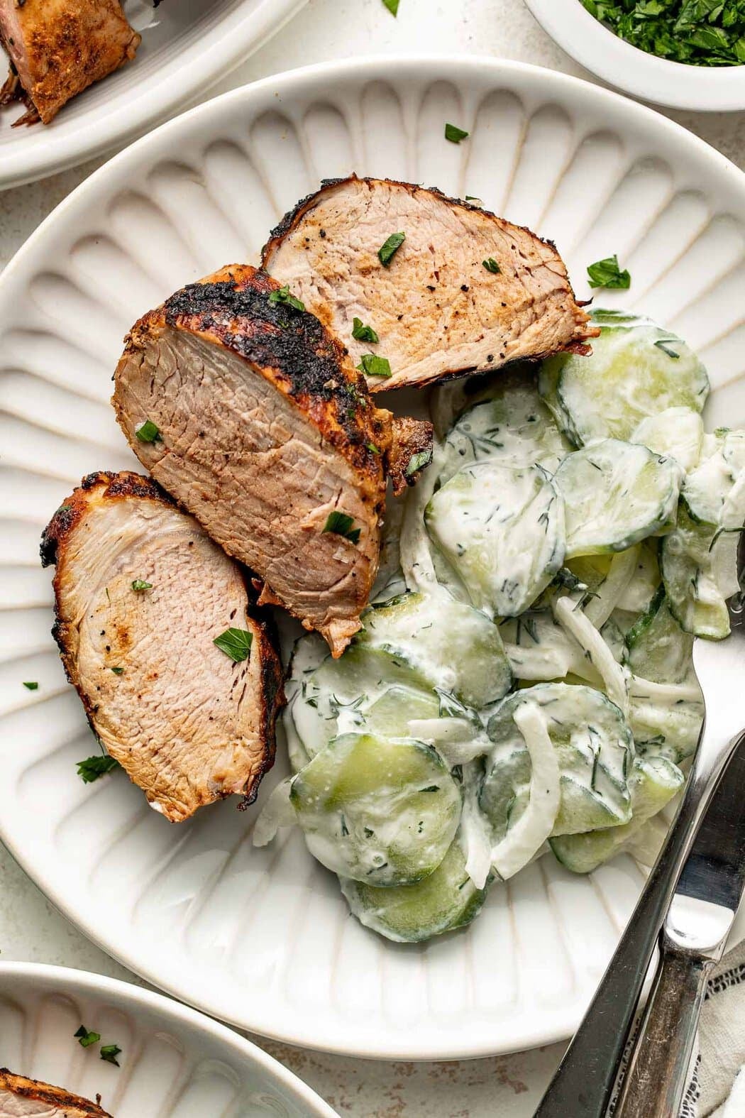 Overhead view of a plate of Creamy Cucumber Salad next to grilled pork loin.