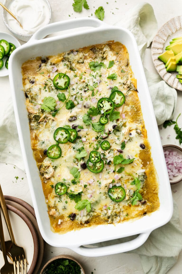 Overhead view of a baking dish filled with a chicken casserole made with green enchilada sauce and topped with fresh jalapeno and melted cheese. 