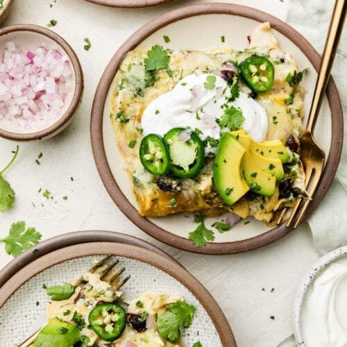 Two plates of servings of green chicken enchilada casserole topped with yogurt and avocado slices