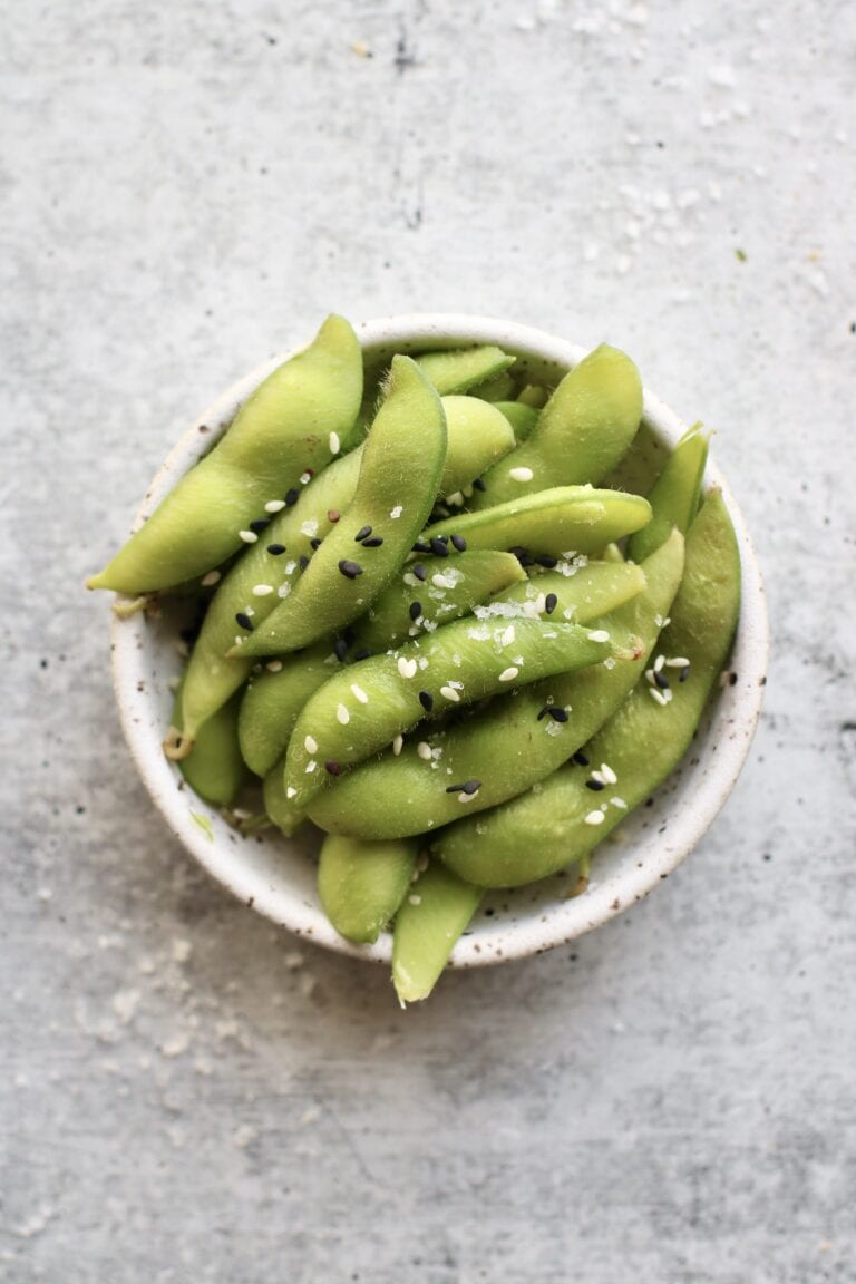 Overhead view of a small bowl of edamame sprinkled with sesame seeds and salt. 