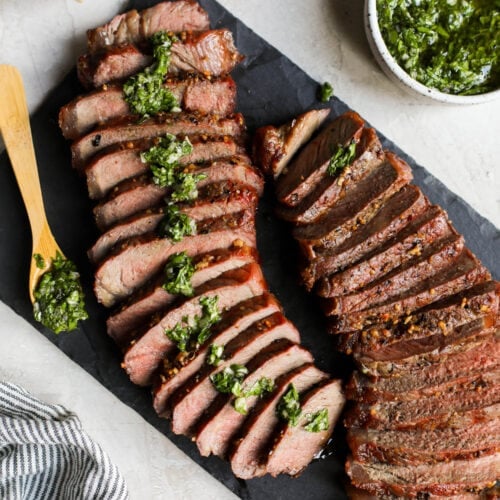 Overhead view black cutting board with grilled and sliced beef roast on top.