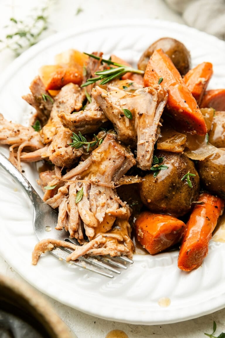 A plate of crock pot pork roast with carrots and potatoes drizzled with gravy and topped with fresh herbs. 