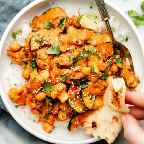 Overhead view vegetarian tikka masala served over rice in bowl, piece of naan being dipped into tikka masala.