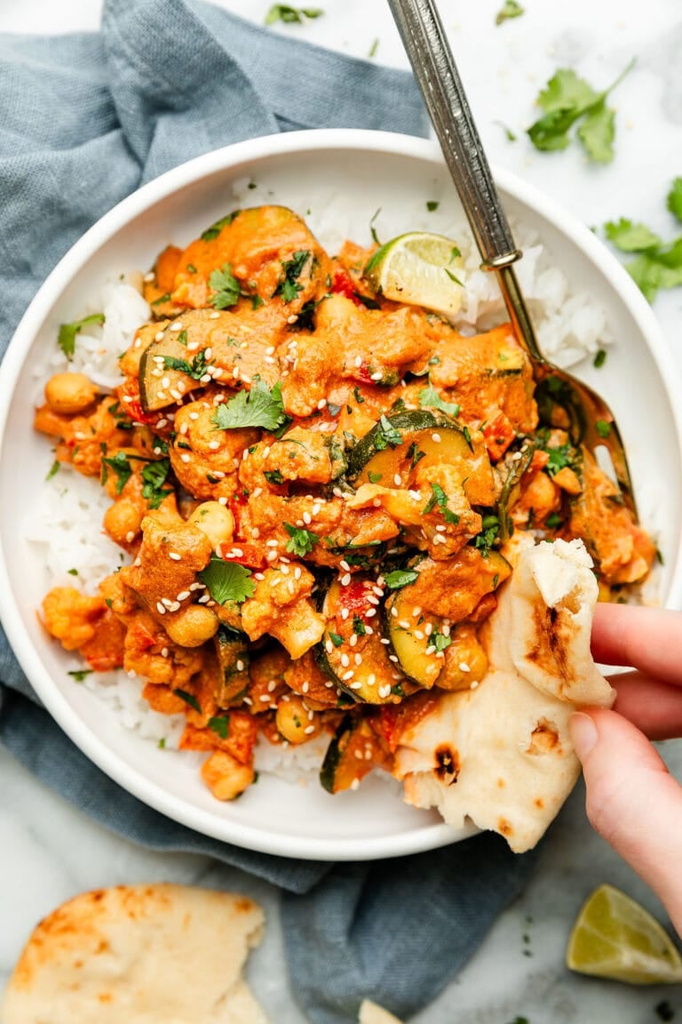 Overhead view of a plate of vegetarian tikka masala being scooped with a piece of naan bread.