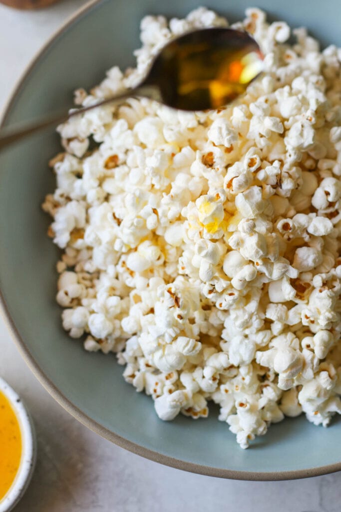A spoonful of melted ghee being drizzled on a bowl of popcorn.