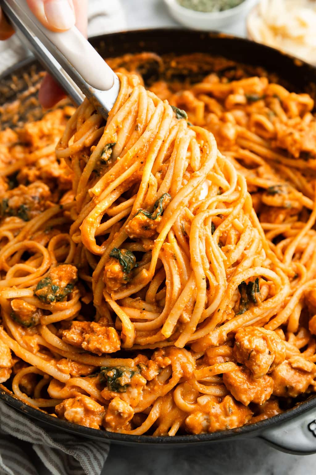 Tongs lifting up twirled pumpkin pasta with sausage and spinach from skillet