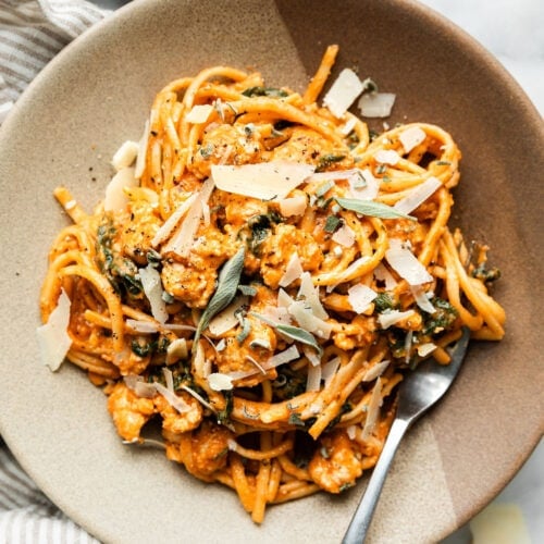Overhead view stone bowl filled with serving of creamy pumpkin pasta with sausage, topped with fresh sage and shaved parmesan