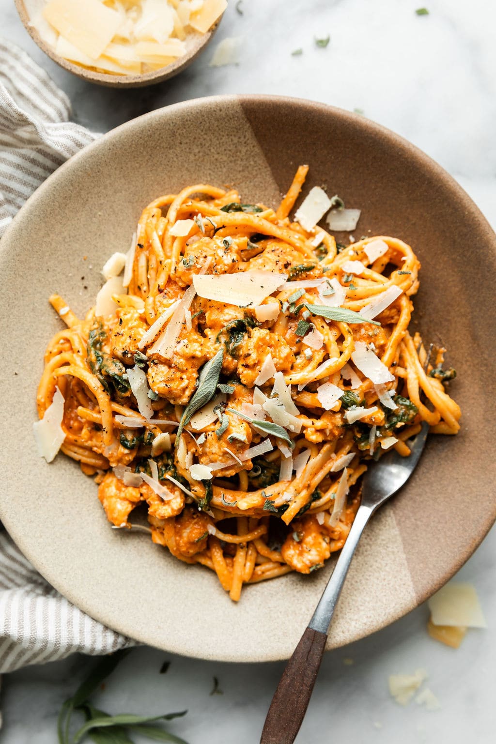 Overhead view creamy pumpkin pasta with sausage, fresh sage, and shaved parmesan in stone bowl