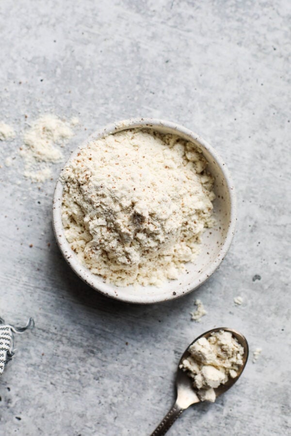 Small bowl filled with protein powder, spoon with small amount protein powder near bowl