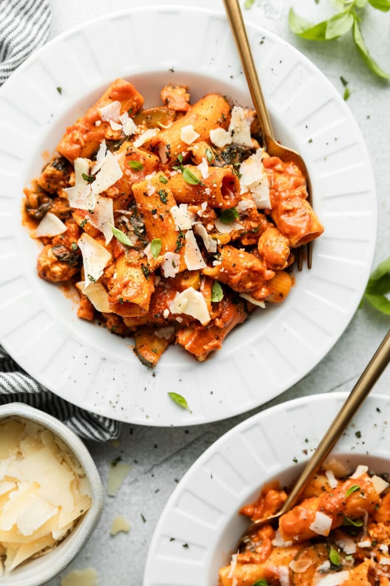 Overhead view of two bowls of rigatoni tossed in a tomato sauce and topped with shaved parmesan cheese and fresh basil. 