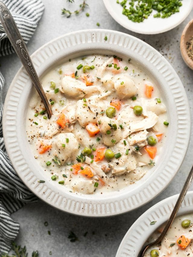 Chicken and dumpling soup served in white bowl with silver spoon