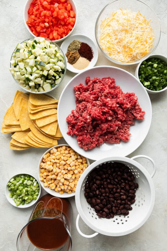 Raw ground beef on white plate with assortment of ingredients. 