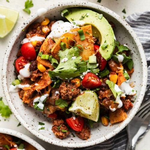 Overhead view serving of enchilada skillet topped with avocado slices, lime wedge and ranch dressing in bowl