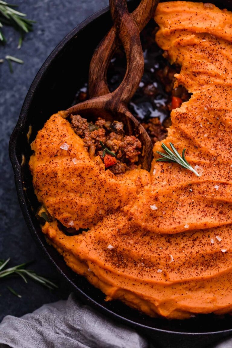Cast Iron skillet filled with sweet potato shepherd's pie being scooped with a wooden spoon. 