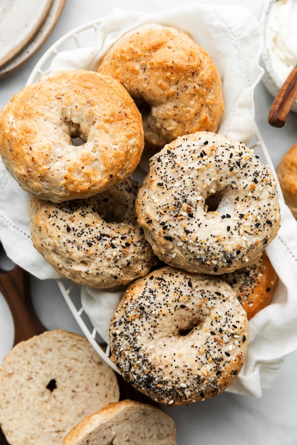 Freshly baked Greek yogurt bagels in a wire basket. Some of the bagels are top with Everything Bagel Seasoning.