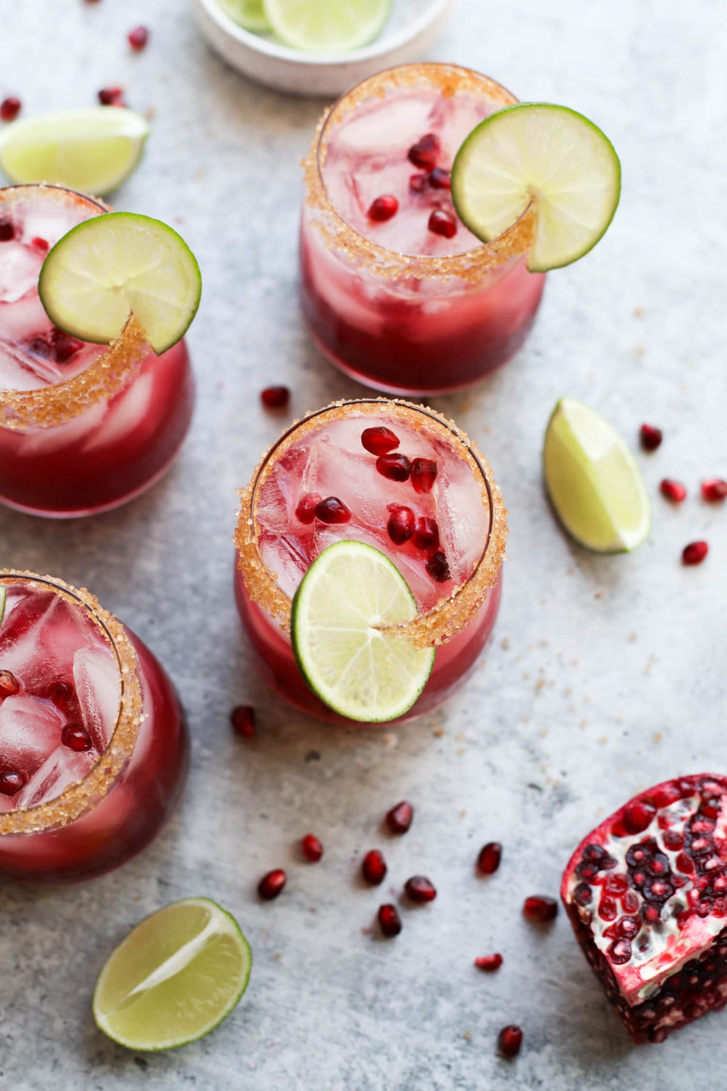 Overhead view three short glasses filled with pomegranate margarita, pomegranate arils floating on top with lime wedge on rims