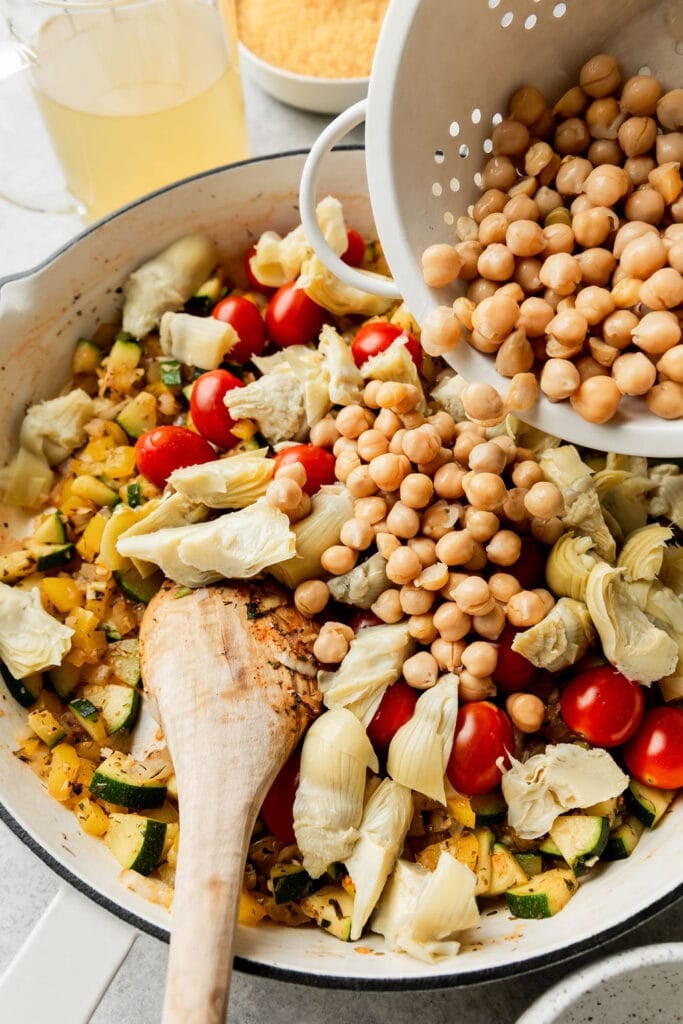Chickpeas being poured into skillet with Greek orzo ingredients