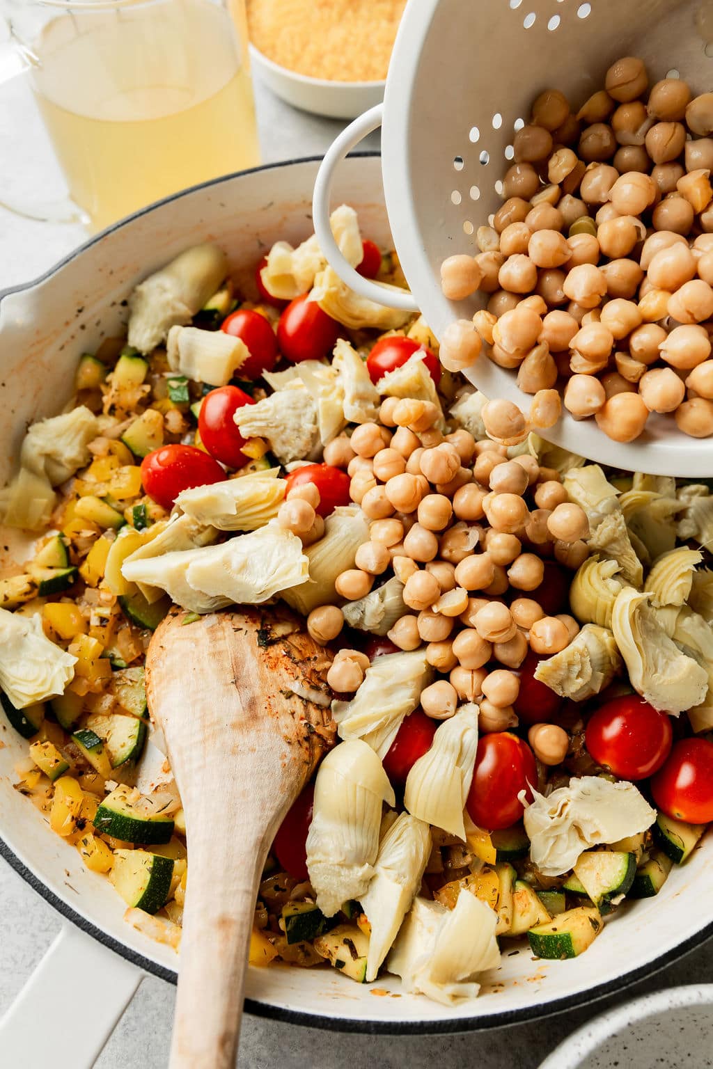 Chickpeas being poured into skillet with Greek orzo ingredients