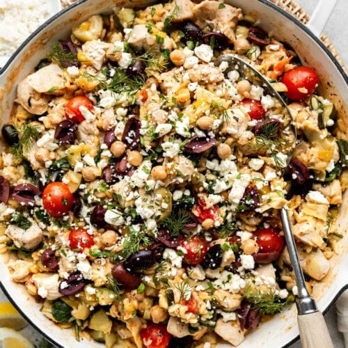 Overhead view white skillet filled with Greek Orzo with chicken and chickpeas, topped with feta cheese and kalamata olives.