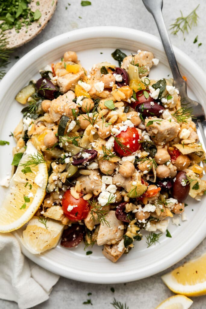 Overhead white plate with serving of Greek Orzo with chicken, chickpeas, and artichokes.