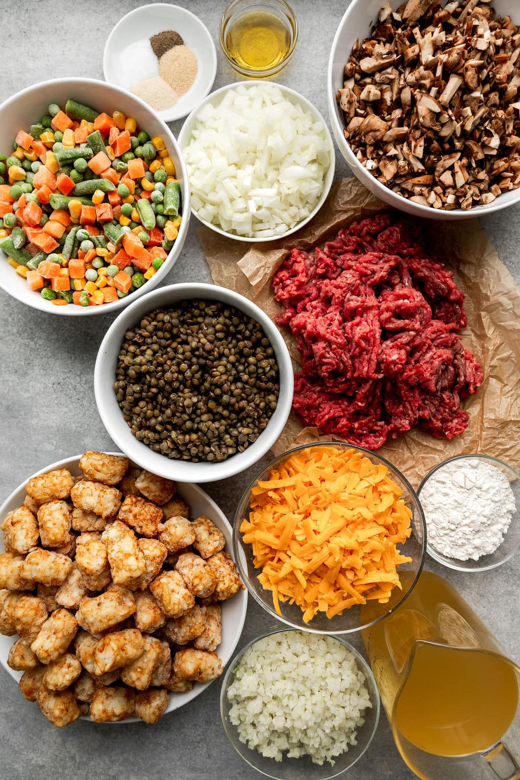 Overhead view of different casserole ingredients in various sized white and clear bowls as well as fresh raw beef.