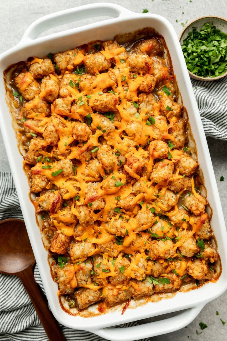 Overhead view of a white casserole dish filled with tater tot hot dish topped with melted cheese and fresh herbs.