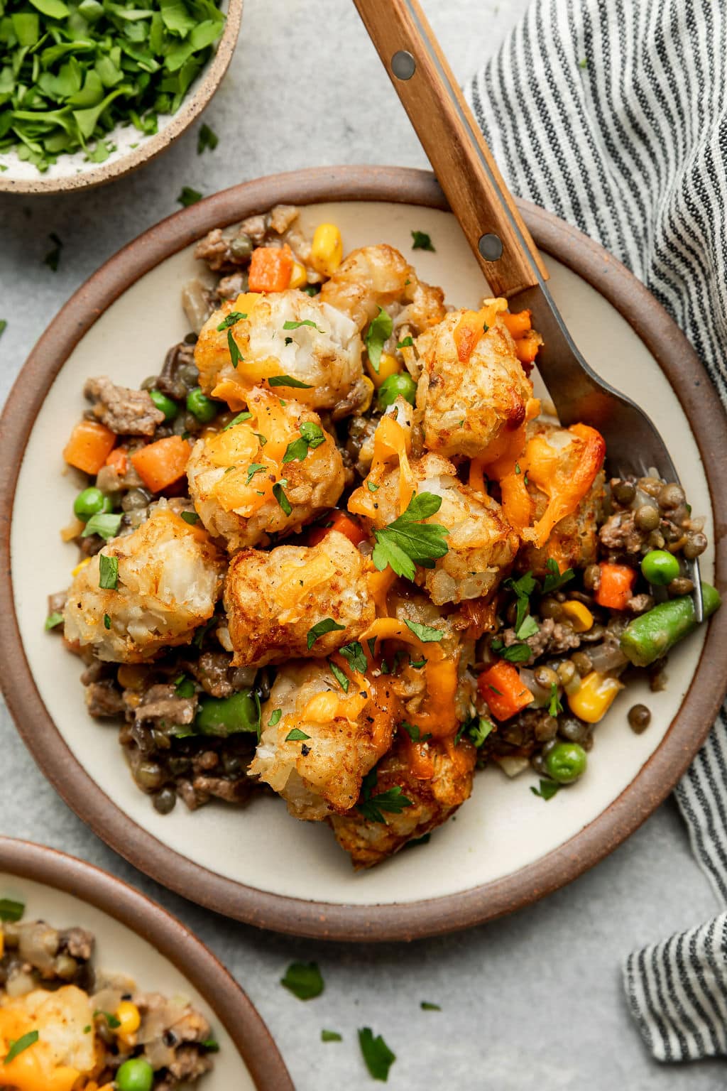 White bowl filled with tater tot hotdish topped with fresh herbs and melted cheese.
