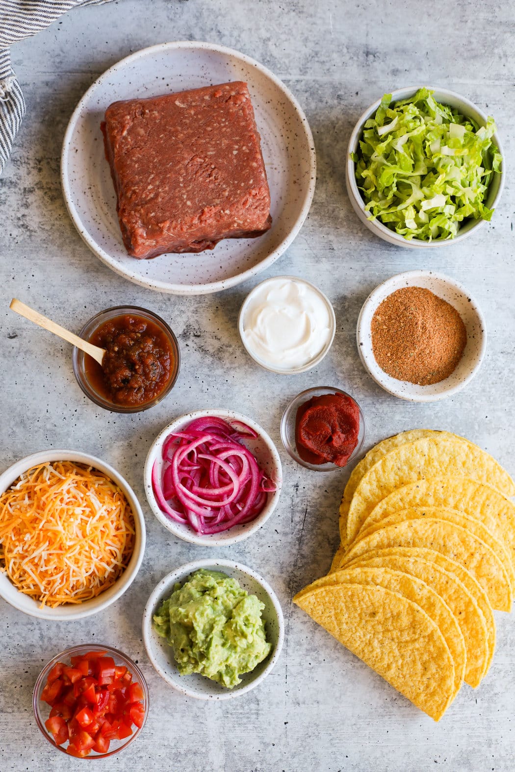 Overhead view of various baked taco ingredients in white bowls of different sizes.