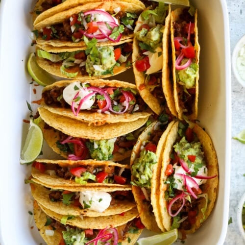 Overhead view white baking dish filled with hard shell tacos filled with beef taco meat, melted cheese and taco toppings