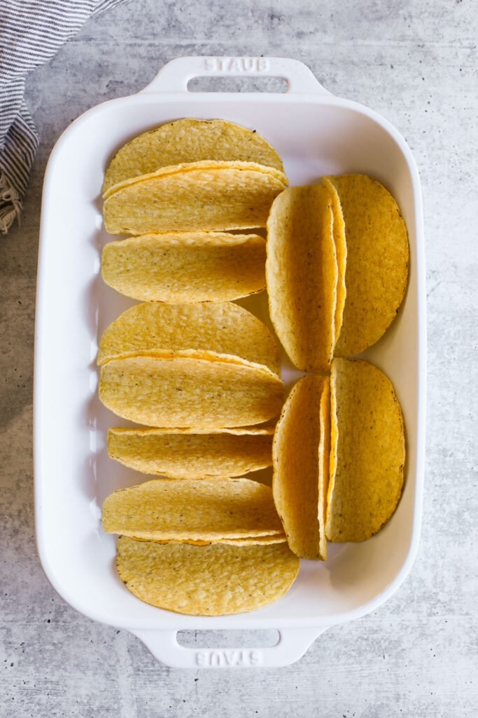 Overhead view of yellow tortilla shells arranged in a white baking dish.