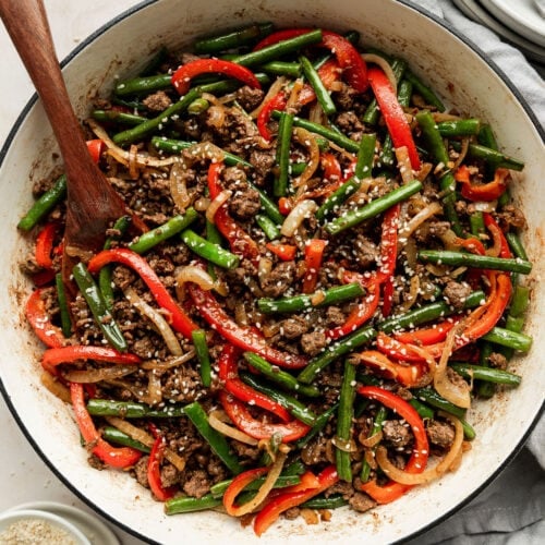 Overhead view of Ground Beef Stir Fry in a white skillet being stirred with a wooden spoon
