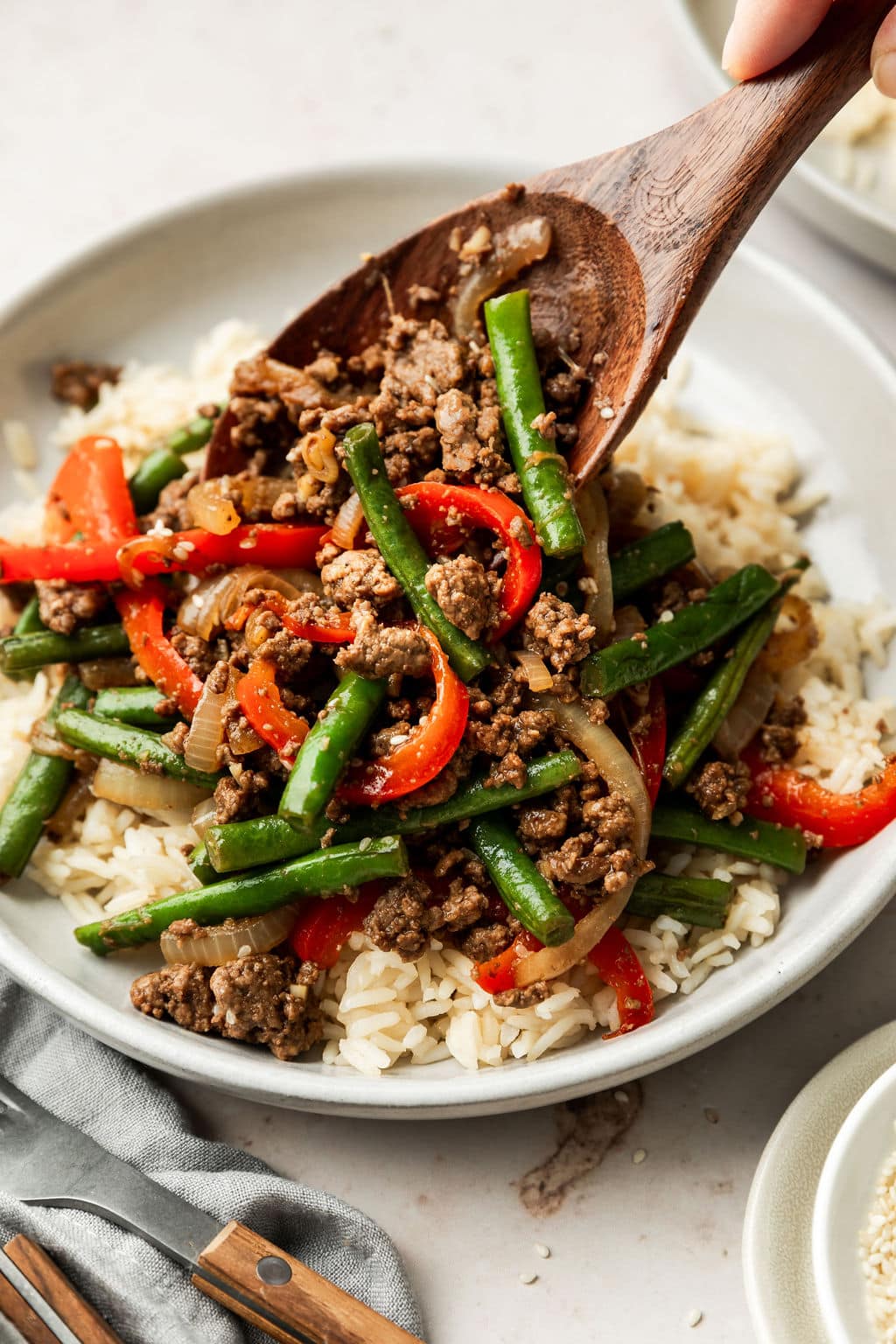 White Bowl containing Ground Beef Stir Fry being scooped with a wooden spoon on top of white rice. 