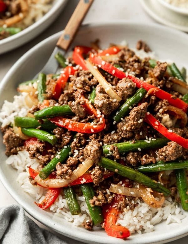 Side view plate filled with ground beef stir fry served over white rice in a bowl