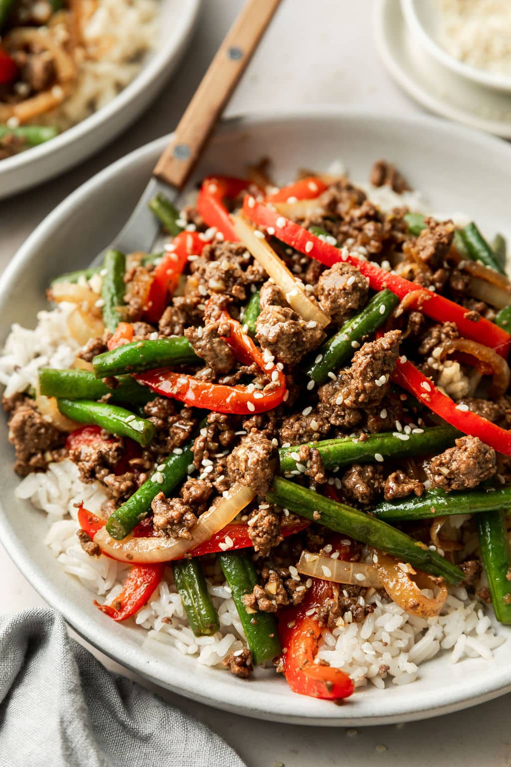 Close up of Ground Beef Stir Fry on a white place on top of white rice and topped with sesame seeds. 